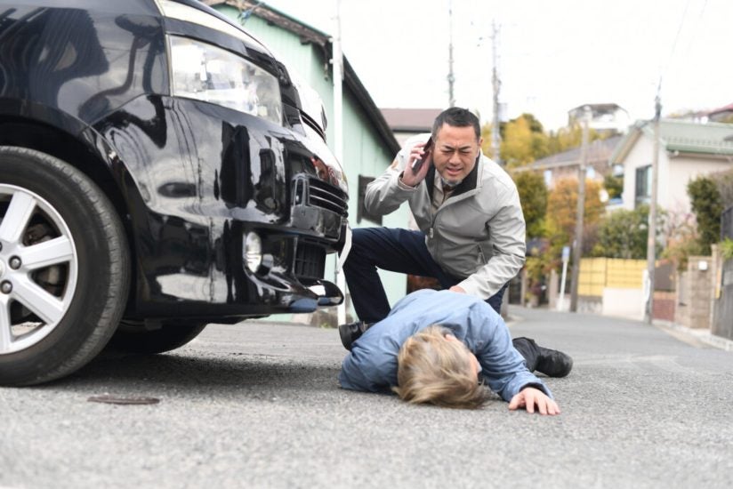 A man lies on the ground beside a car indicating a possible accident in Riverside, CA